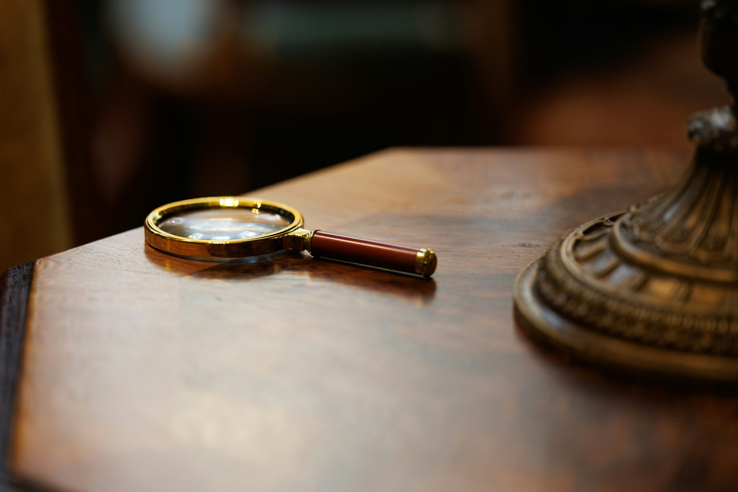 薄暗い書斎のデスクに置かれた調査報告書と虫眼鏡のイメージ